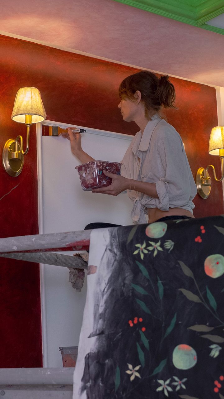 Artist working beside brass wall lights on a crimson wall