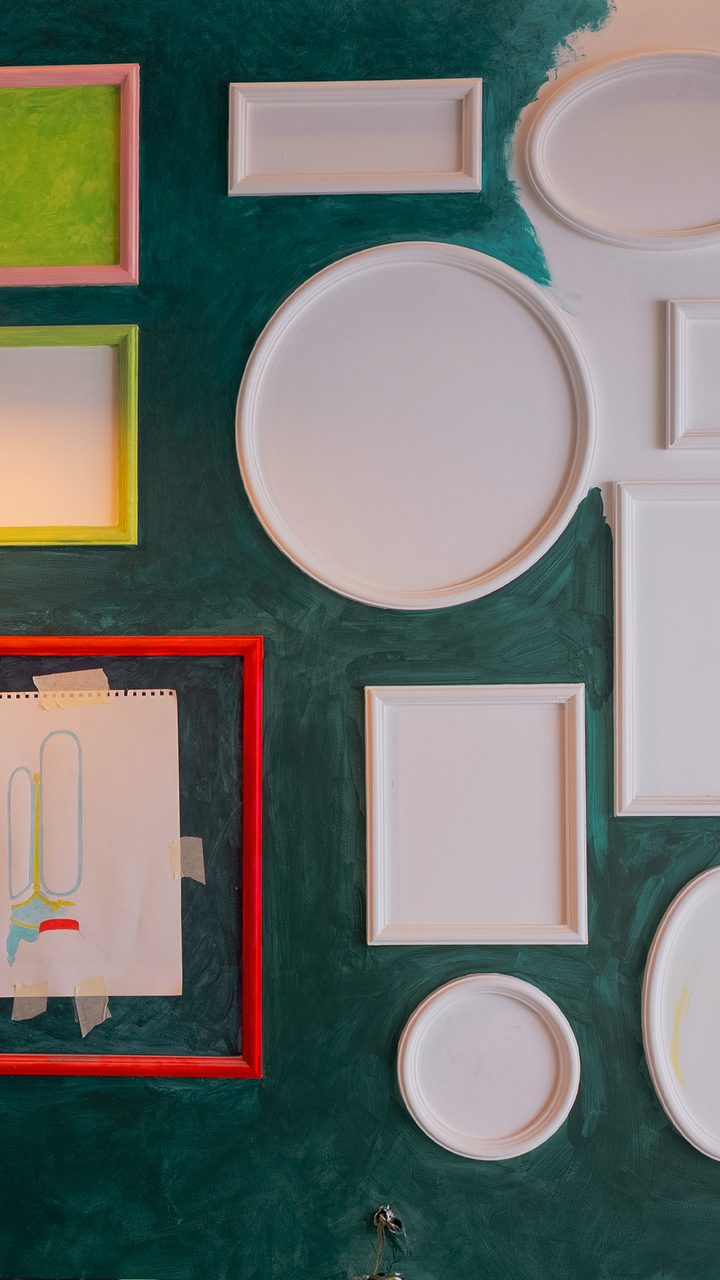 Wall of white frames and mouldings on hand painted green
