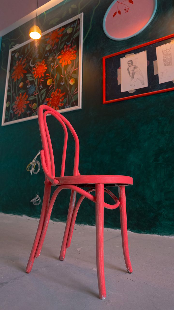 A coral painted bentwood chair against a deep green wall with framed floral artwork