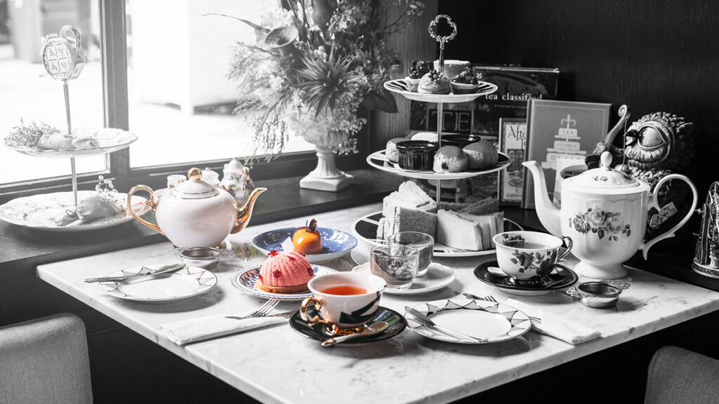 English afternoon tea setup with teapots, desserts, sandwiches, and fine china by a window in Dubai hotel restaurant